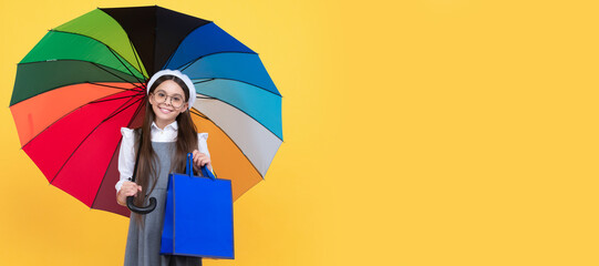 happy teen girl under colorful umbrella in autumn season hold shopping bag, autumn sale. Child with autumn umbrella, rainy weather, horizontal poster, banner with copy space.