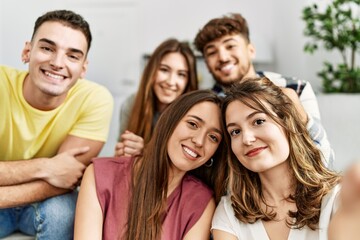 Group of young friends smiling happy make selfie by the smartphone sitting on the sofa at home.