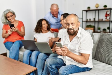 Group of middle age friends using laptop and smartphone sitting on the sofa at home.