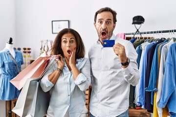 Hispanic middle age couple holding shopping bags and credit card afraid and shocked, surprise and amazed expression with hands on face