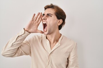 Young man standing over isolated background shouting and screaming loud to side with hand on mouth....