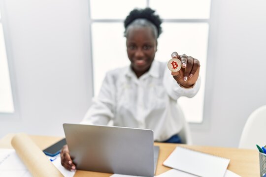 Young african american woman architect using laptop holding bitcoin at architecture studio