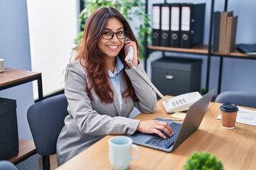 Young hispanic woman business worker using laptop talking on the telephone at office