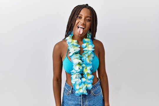 Young african american woman with braids wearing bikini and hawaiian lei sticking tongue out happy with funny expression. emotion concept.