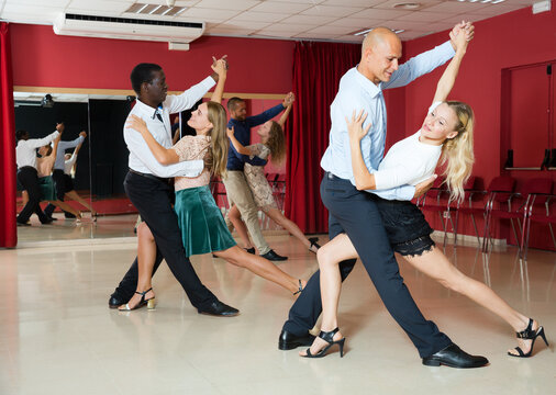 Young positive people dancing samba in pairs in dance hall..