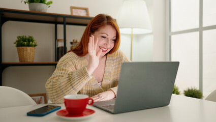 Fototapeta premium Young redhead woman having video call sitting on table at home