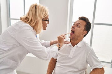 Middle age man and woman doctor and patient examining throat having medical consultation at clinic