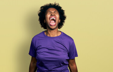 African american woman with afro hair wearing casual purple t shirt angry and mad screaming...