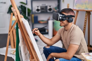 Fototapeta na wymiar Young hispanic man artist using virtual reality glasses drawing at art studio