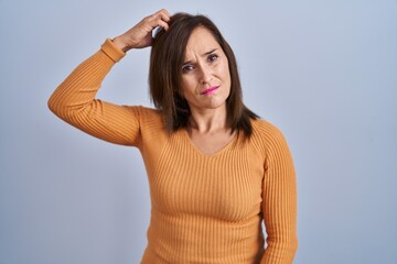 Middle age brunette woman standing wearing orange sweater confuse and wondering about question....