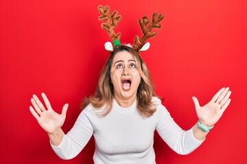 Middle age caucasian woman wearing cute christmas reindeer horns crazy and mad shouting and yelling...