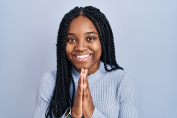 Fototapeta na wymiar African american woman standing over blue background praying with hands together asking for forgiveness smiling confident.
