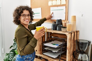 Young hispanic woman drinking coffee pointing with finger to document at office