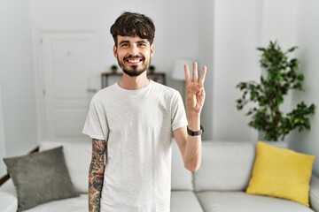 Hispanic man with beard at the living room at home showing and pointing up with fingers number...