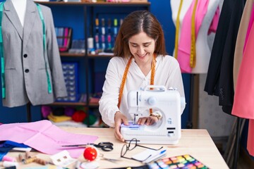 Young woman tailor smiling confident using sewing machine at sewing studio