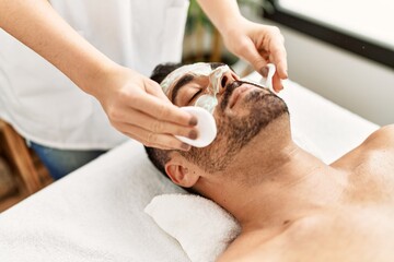 Obraz na płótnie Canvas Young hispanic man having facial mask treatment at beauty center
