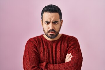 Young hispanic man with beard wearing casual sweater over pink background skeptic and nervous,...