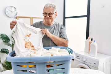 Senior caucasian man holding dirty t shirt with stain smiling with a happy and cool smile on face. showing teeth.