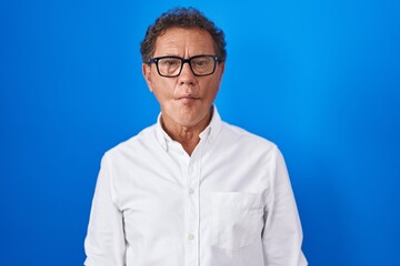 Obraz premium Middle age hispanic man standing over blue background making fish face with lips, crazy and comical gesture. funny expression.