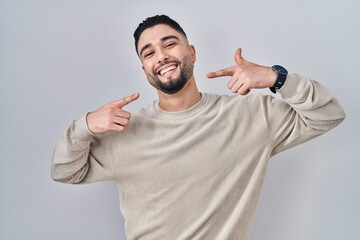 Young handsome man standing over isolated background smiling cheerful showing and pointing with...