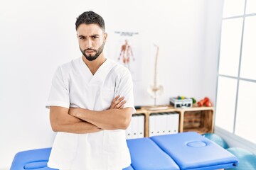 Obraz premium Young handsome man with beard working at pain recovery clinic skeptic and nervous, disapproving expression on face with crossed arms. negative person.
