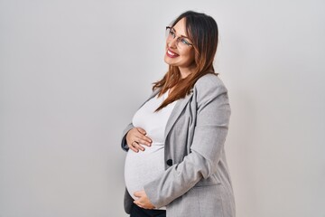 Pregnant business woman standing over white background looking away to side with smile on face, natural expression. laughing confident.