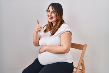 Pregnant woman wearing band aid for vaccine injection smiling happy and positive, thumb up doing excellent and approval sign