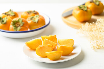 Sliced ripe persimmon fruit on plate with white background