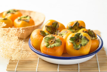 Ripe persimmon fruit in bowl on white background