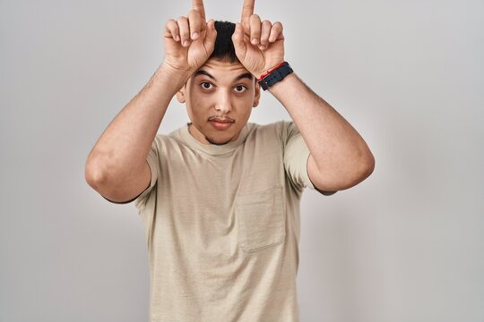 Young arab man wearing casual t shirt doing funny gesture with finger over head as bull horns