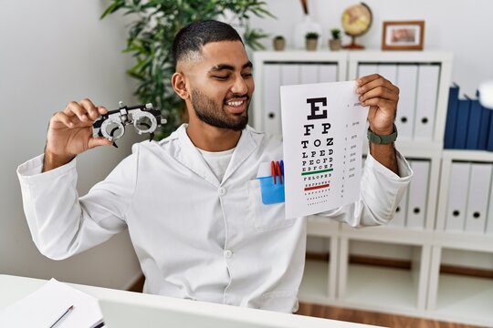 Young arab man holding sneller test and optometry glasses at clinic
