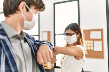 Two business workers wearing medical mask doing elbow coronavirus handshake at the office.
