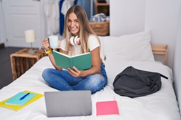 Young beautiful hispanic woman student reading book and drinking coffee at bedroom