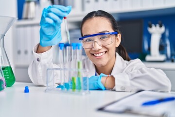 Young hispanic woman scientist measuring liquid at laboratory