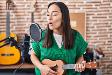 Fototapeta na wymiar Young hispanic woman musician singing song playing ukulele at music studio