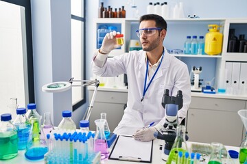 Young hispanic man scientist looking urine test tube writing report at laboratory