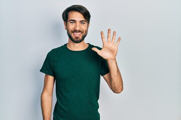 Young hispanic man wearing casual white tshirt showing and pointing up with fingers number five while smiling confident and happy.