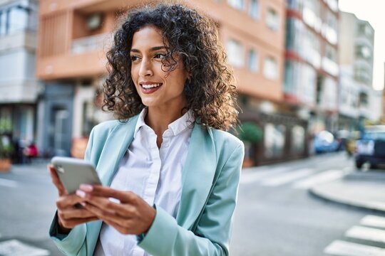 Young hispanic business woman wearing professional look smiling confident at the city using smartphone