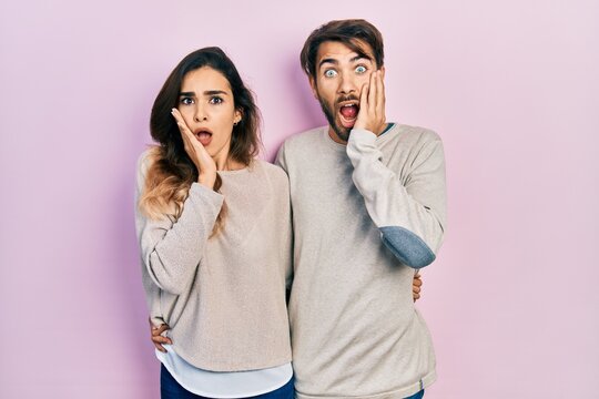 Young hispanic couple wearing casual clothes afraid and shocked, surprise and amazed expression with hands on face