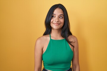 Obraz premium Brunette woman standing over yellow background smiling looking to the side and staring away thinking.