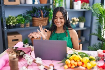 Brunette woman working at florist shop doing video call doing ok sign with fingers, smiling friendly gesturing excellent symbol