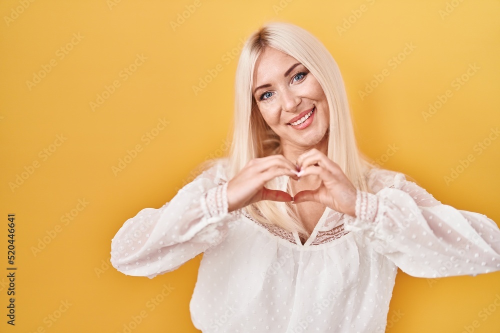 Poster caucasian woman standing over yellow background smiling in love showing heart symbol and shape with 