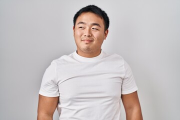 Young chinese man standing over white background smiling looking to the side and staring away thinking.