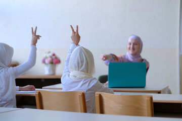 Diversity of Muslim school students raises their hands to answer teacher questions. 