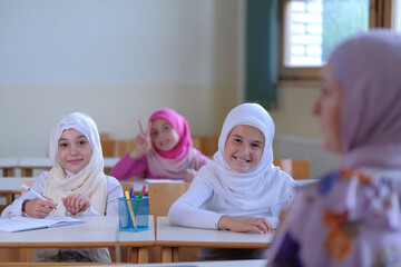 Group of Muslim school children sitting at the school desk in the classroom during class listening...