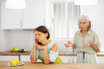 Senior woman scolding her adult daughter cooking breakfast in kitchen