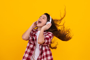Fototapeta premium Amazed teenager. Teenager child girl in headphones listening music, wearing stylish casual outfit isolated over yellow background. Excited teen girl.