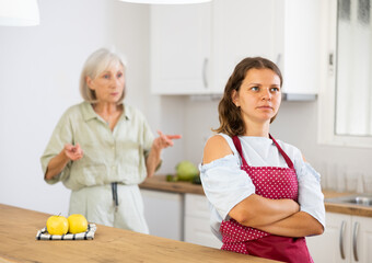 Upset young girl at home kitchen while worried elderly mother reprimanding her. Family conflicts concept