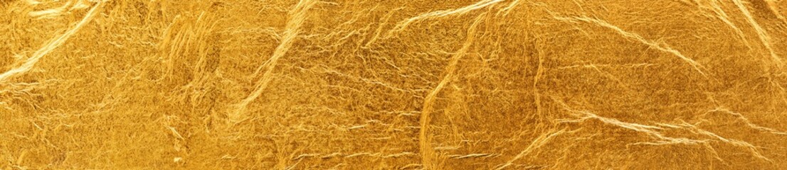 Shiny gold background made of rough textured gold leaf.