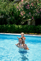 Smiling dad standing in the pool with a small child on his shoulders